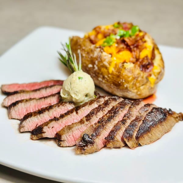 Sliced steak with herb butter and a loaded baked potato with cheese, bacon, and chives.