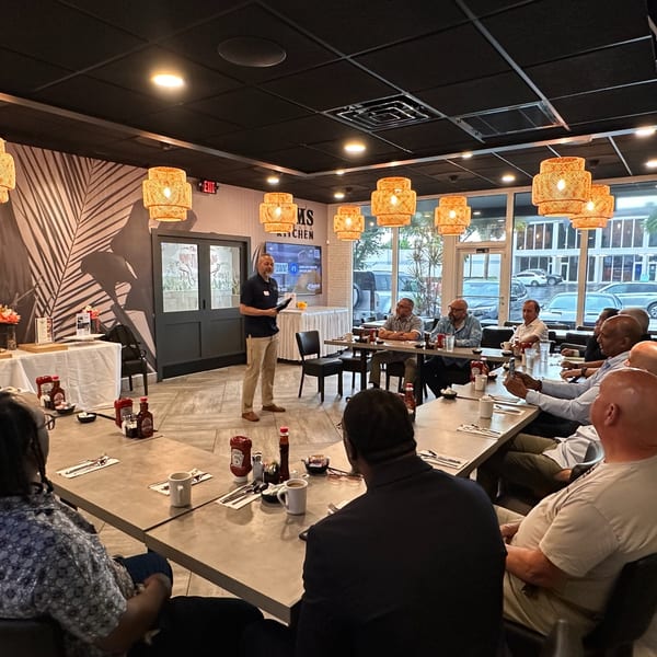 A man speaks to a group of men seated at tables in Mom's Kitchen restaurant.