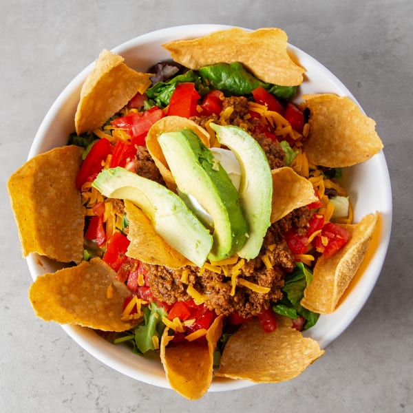 Taco salad with ground beef, lettuce, tomatoes, cheese, avocado, sour cream, and tortilla chips.