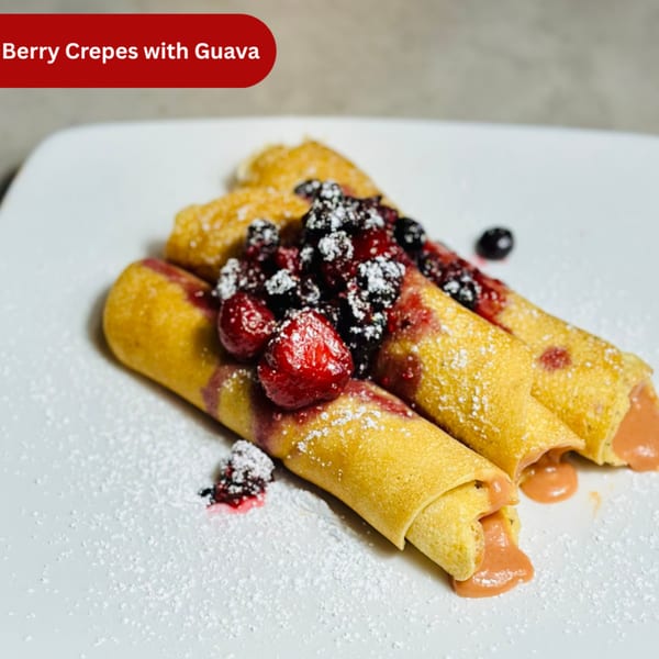 Three golden crepes filled with guava, topped with mixed berries and powdered sugar on a white plate.