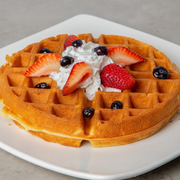 Golden waffle topped with whipped cream, fresh strawberries, and blueberries on a white plate.