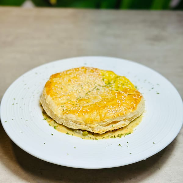 Golden-brown puff pastry pie, topped with sesame seeds and herbs, served on a white plate.