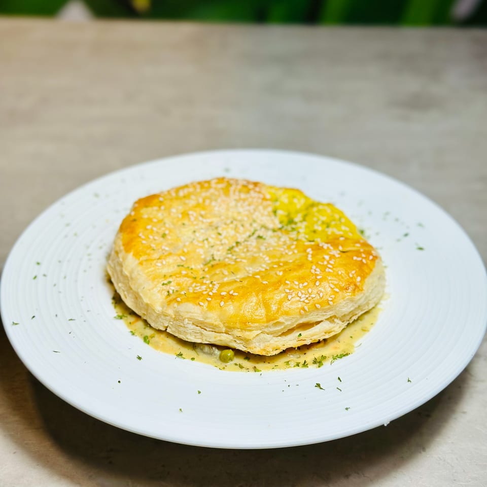 Golden-brown puff pastry pie, topped with sesame seeds and herbs, served on a white plate.