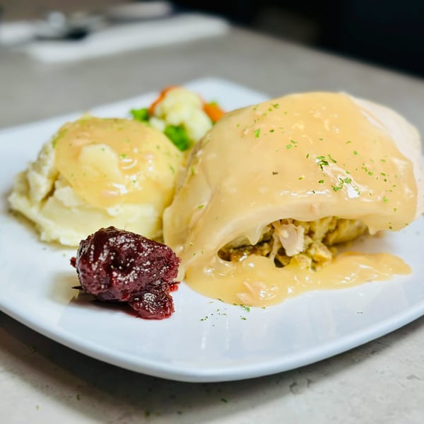 Turkey breast with gravy, mashed potatoes, cranberry sauce, and mixed vegetables on a white plate.