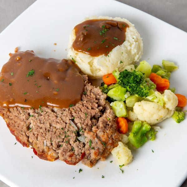 Meatloaf with gravy, mashed potatoes, and mixed vegetables on a white plate.