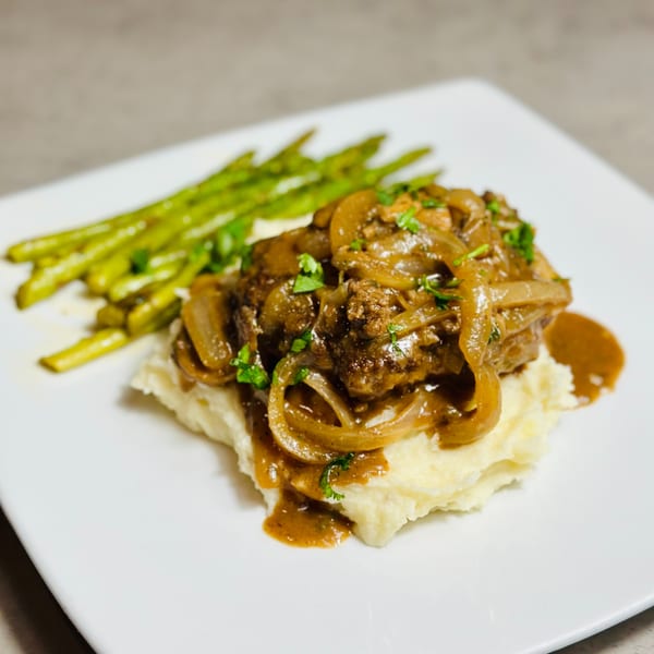 Savory steak with caramelized onions and gravy, served over mashed potatoes with a side of asparagus.