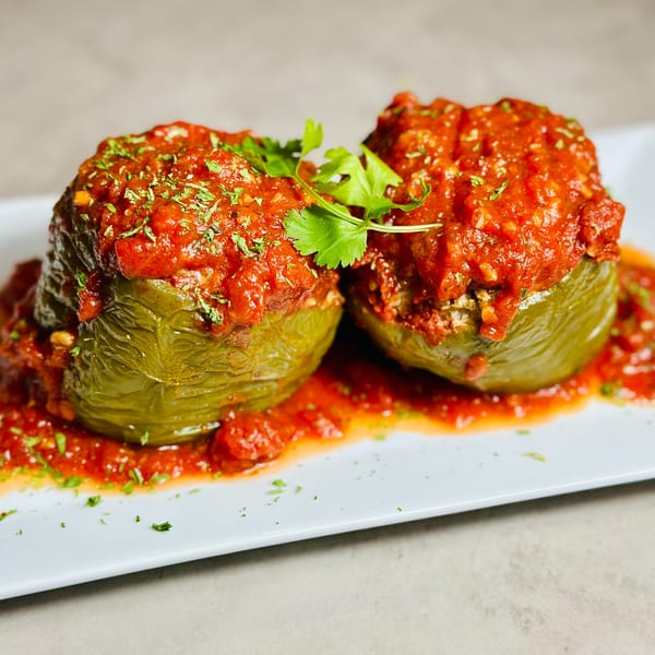 Two stuffed green bell peppers topped with red sauce and fresh parsley on a white plate.