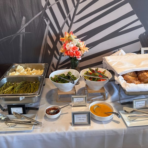 A buffet table at Mom's Kitchen with mashed potatoes, asparagus, salads, dressing, and assorted breads.