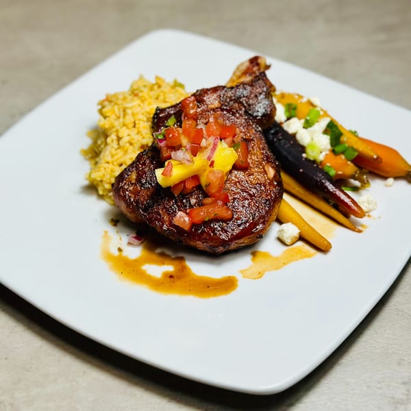 Glazed chicken with mango salsa, yellow rice, and roasted carrots with feta on a white plate.