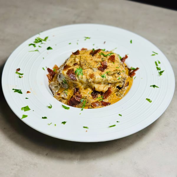 Savory breakfast dish from Mom's Kitchen, topped with creamy sauce, bacon, and fresh parsley.