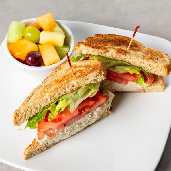 Tuna salad sandwich on toasted bread with lettuce, tomato, and a side of fruit salad.