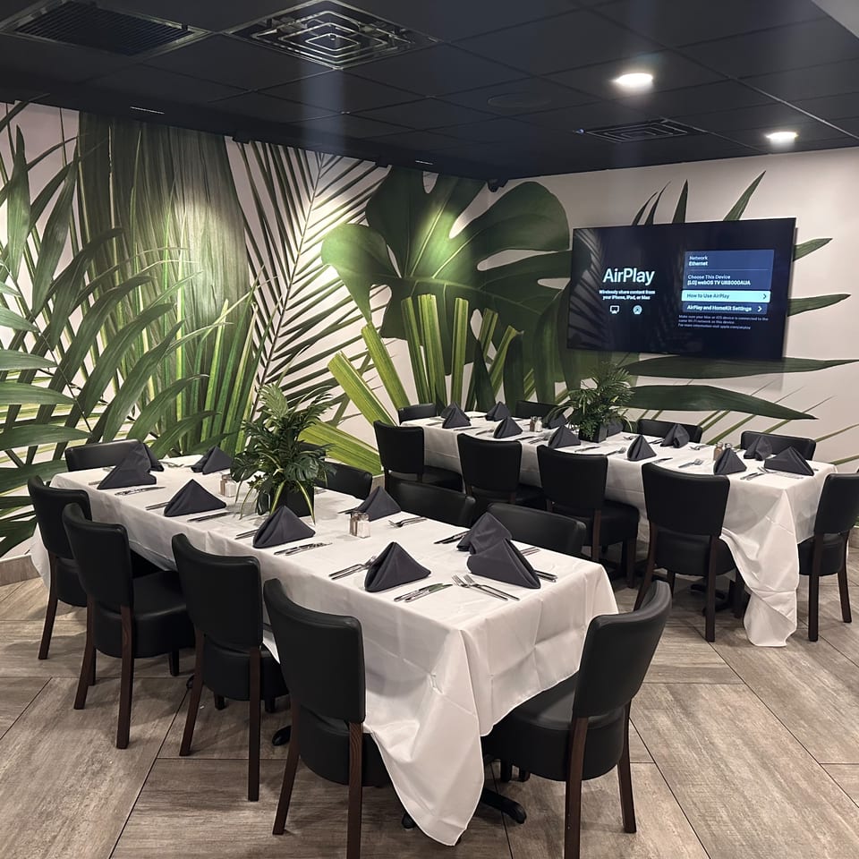 A dining room at Mom's Kitchen with tables set with white tablecloths, black napkins, and tropical leaf wallpaper.